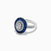 The Royal Bleu 14K White Gold Sapphire and Diamond Ring showcases an oval diamond cluster center, haloed by blue sapphires and accented with diamonds on the shoulders.