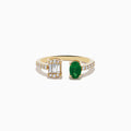 The 14K Yellow Gold Emerald and Diamond Toi Et Moi Ring features a row of diamonds on the band, an emerald-cut diamond cluster on one side, and a striking green oval emerald gemstone on the other.
