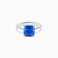 The Nahla 14K White Gold Cushion Tanzanite and Diamond Ring features a large cushion-cut blue tanzanite, flanked by sparkling diamonds along the band, shown on a white background.