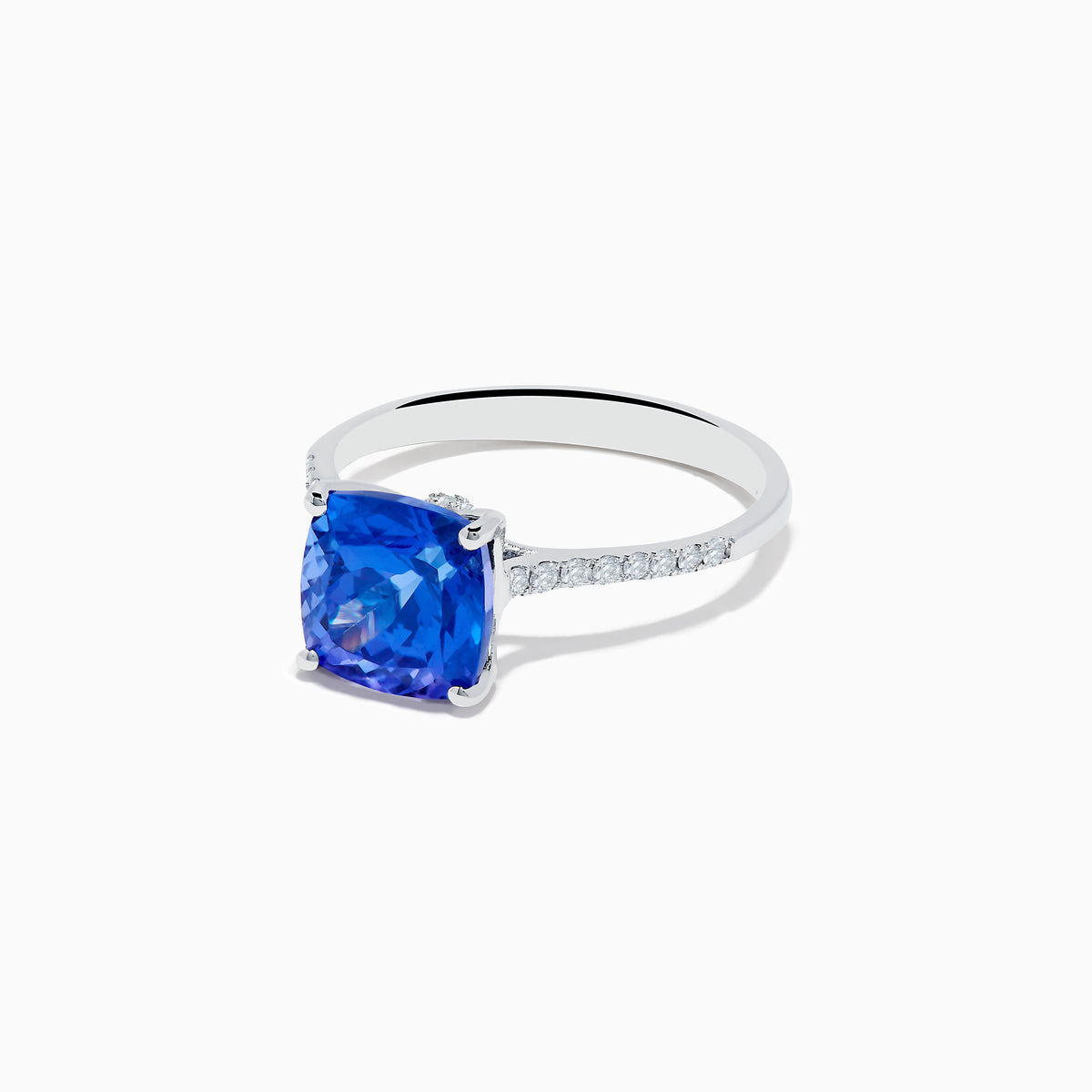 The Nahla 14K White Gold Cushion Tanzanite and Diamond Ring features a large cushion-cut blue tanzanite, flanked by sparkling diamonds along the band, shown on a white background.