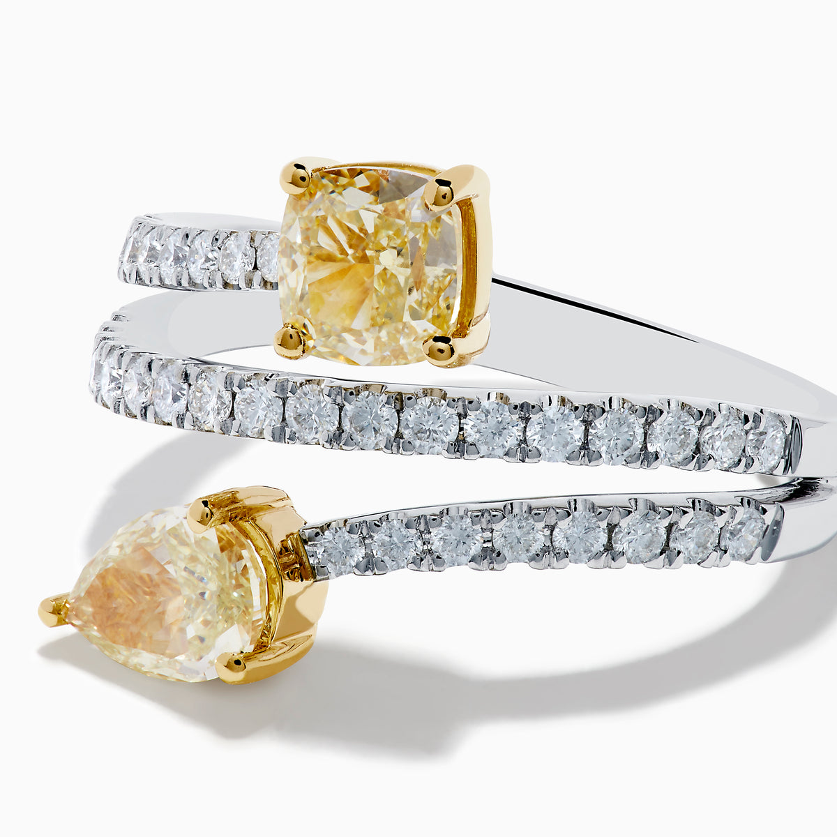 The Canare 18K Two Tone White and Yellow Diamond Bypass Ring features a spiral design with a row of small white diamonds, highlighted by yellow cushion-cut and pear-shaped diamonds set in yellow gold prongs.