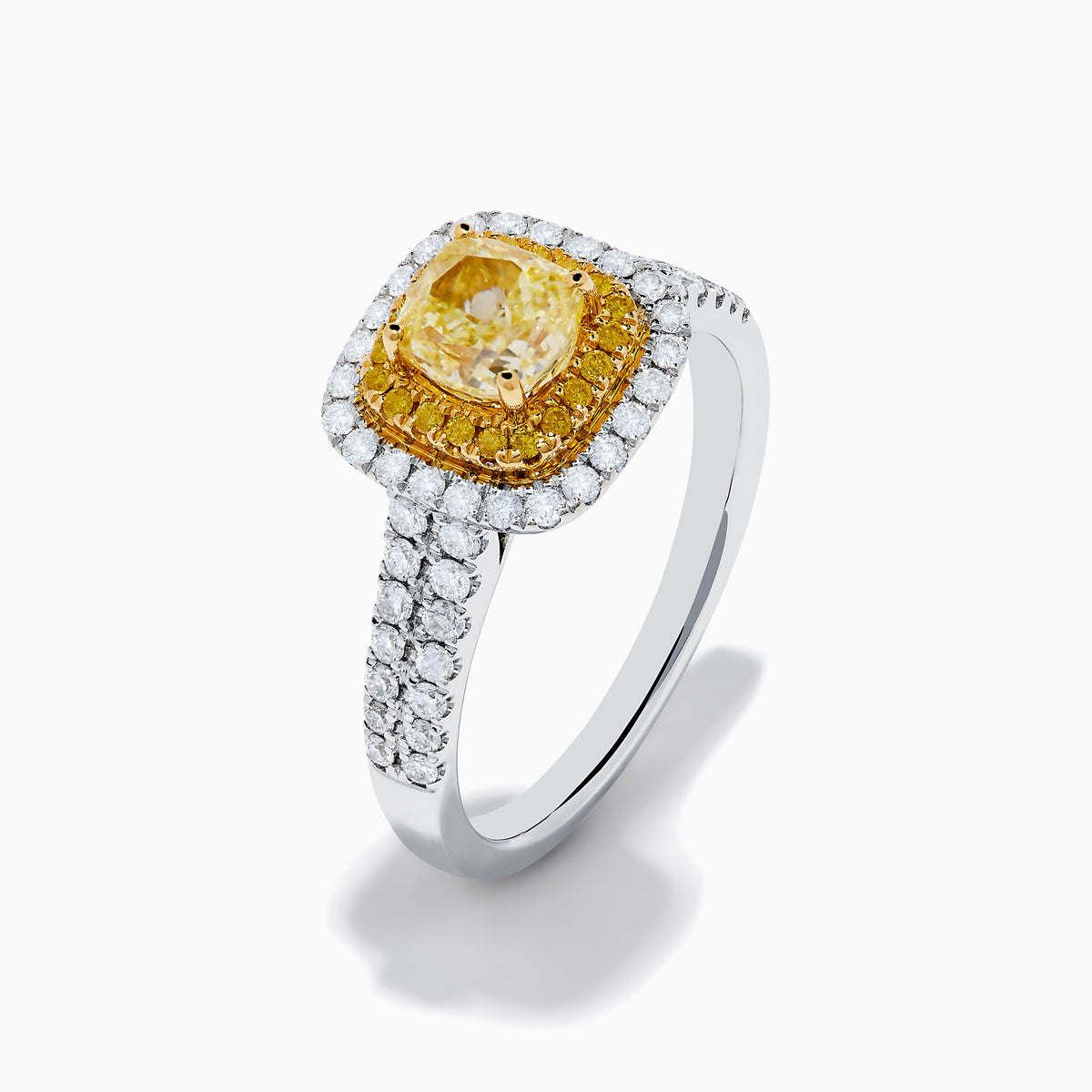 The Canare 18K Two Tone White and Yellow Diamond Ring showcases a square yellow center stone, encircled by yellow and white diamond halos, set on a band adorned with sparkling clear diamonds.
