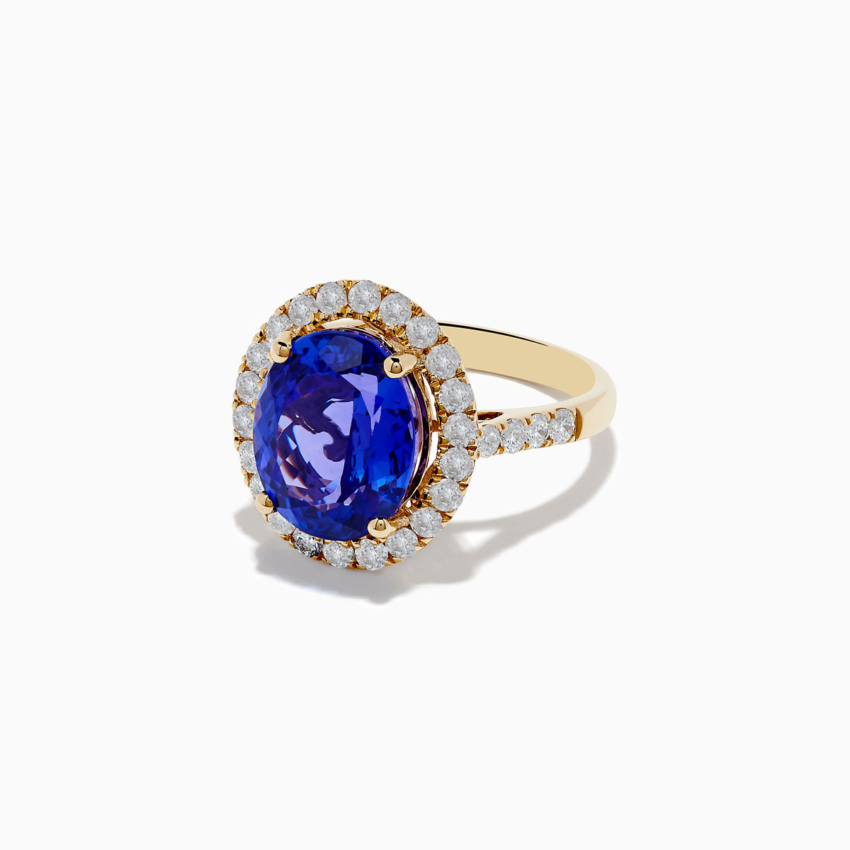 The Nahla Siri 14K Yellow Gold Tanzanite and Diamond Ring features a large oval blue tanzanite center stone encircled by a halo of small round white diamonds, displayed on a plain white background.