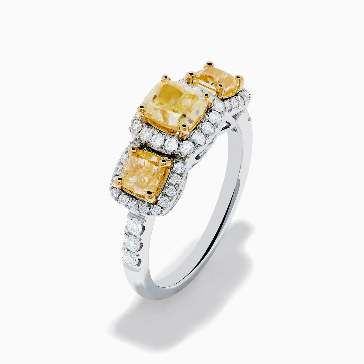 The Canare 18K Two Tone White and 3 Stone Yellow Diamond Ring showcases three rectangular yellow diamonds, each haloed with sparkling diamonds, set on a diamond-studded white gold band.