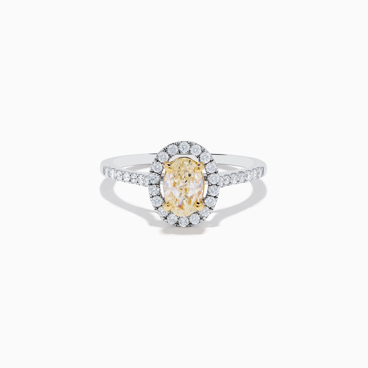 The Canare 18K Two Tone White and Yellow Diamond Ring features an oval yellow diamond center, surrounded by a halo of round white diamonds with extra diamonds adorning the band.