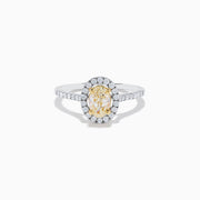 The Canare 18K Two Tone White and Yellow Diamond Ring features an oval yellow diamond center, surrounded by a halo of round white diamonds with extra diamonds adorning the band.