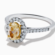 The Canare 18K Two Tone White and Yellow Diamond Ring features an oval yellow diamond center, surrounded by a halo of round white diamonds with extra diamonds adorning the band.