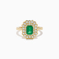 The Brasilica 14K Yellow Gold Emerald and Diamond Double Halo Ring showcases a rectangular green emerald at the center, accented by two rows of sparkling round white diamonds in an elegant scalloped halo design.