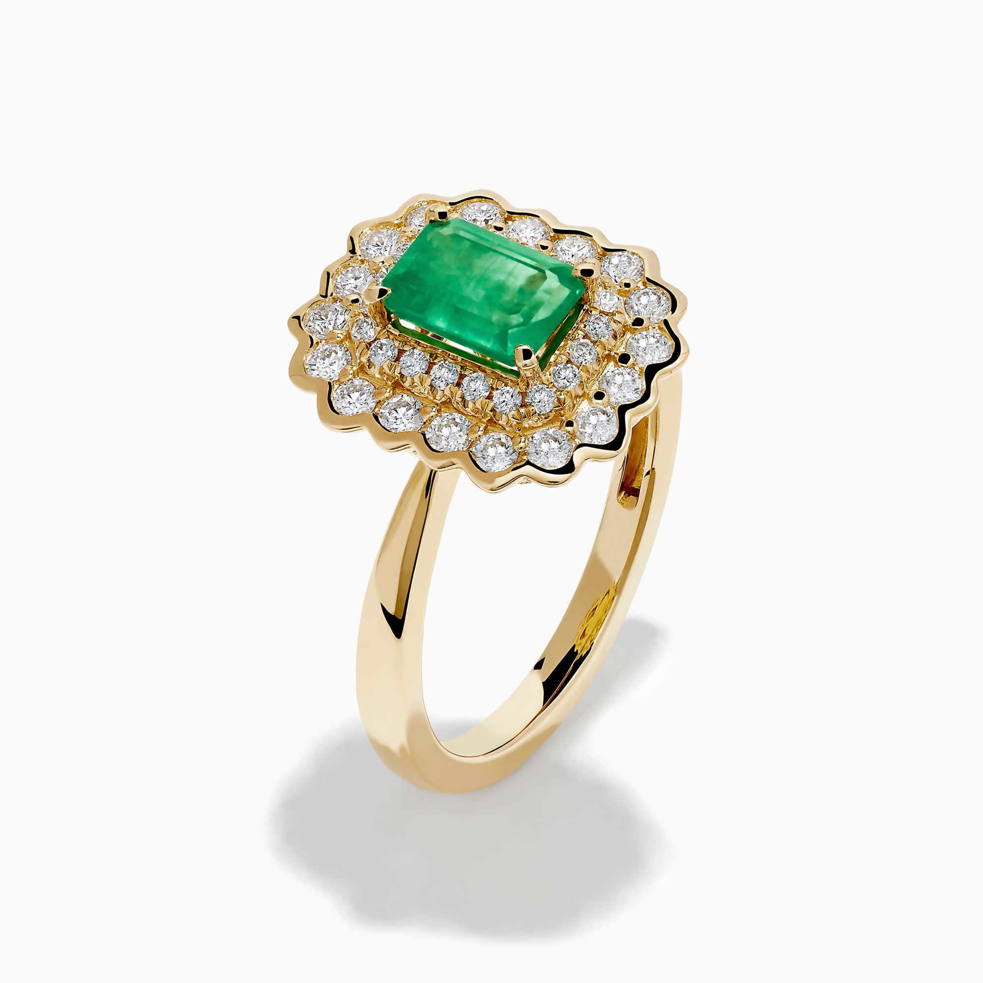 The Brasilica 14K Yellow Gold Emerald and Diamond Double Halo Ring showcases a rectangular green emerald at the center, accented by two rows of sparkling round white diamonds in an elegant scalloped halo design.