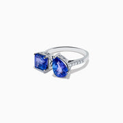The Nahla Siri 14K White Gold Tanzanite and Diamond Toi Et Moi Ring features two blue tanzanite stones—one square-cut, one pear-shaped—side by side with diamond accents on the band, shown on a white background.