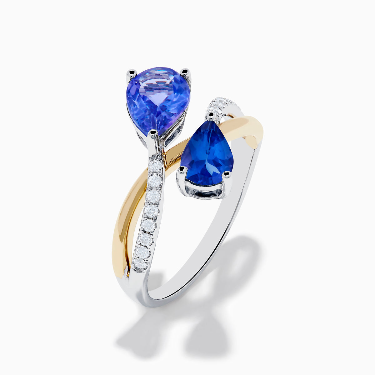 The Nahla 14K Two Tone Gold Tanzanite and Diamond Bypass Ring features two pear-shaped tanzanites and a curved band with sparkling white diamonds, displayed against a white background.