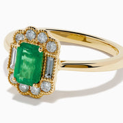 The 14K Yellow Gold Emerald and Diamond Halo Vintage Ring features an emerald-cut green center stone, accented by round and baguette white diamonds in a vintage halo setting.