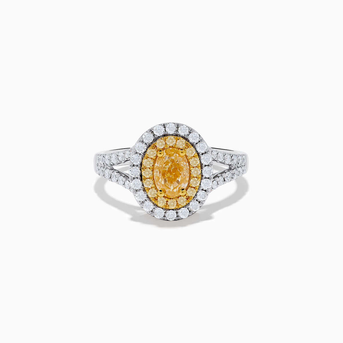 The Canare 18K Two Tone Gold White and Yellow Oval Diamond Split Shank Ring showcases an oval yellow diamond center with a double halo of white diamonds and a diamond-accented split shank, displayed on a plain white background.