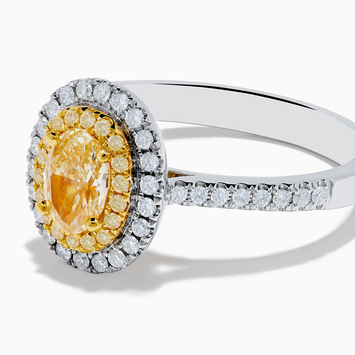 The Canare 18K Two Tone Gold White & Yellow Diamond Ring features a central oval yellow gemstone, accented by a halo of white diamonds and additional diamonds set along the band.