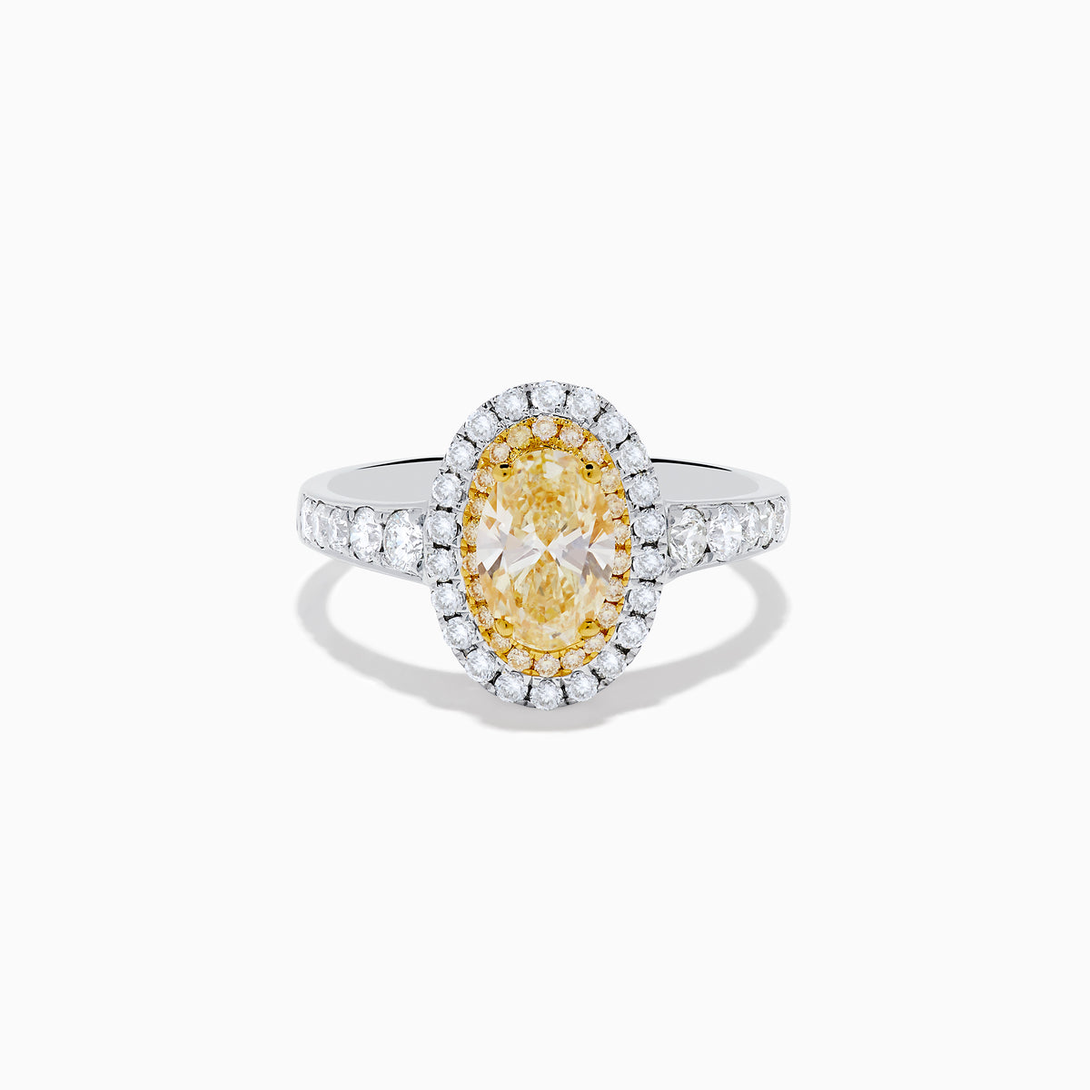 The Canare 18K Two Tone Gold White and Yellow Oval Diamond Ring features a large yellow diamond at the center, a halo of small round white diamonds, and additional diamonds set along the elegant band.