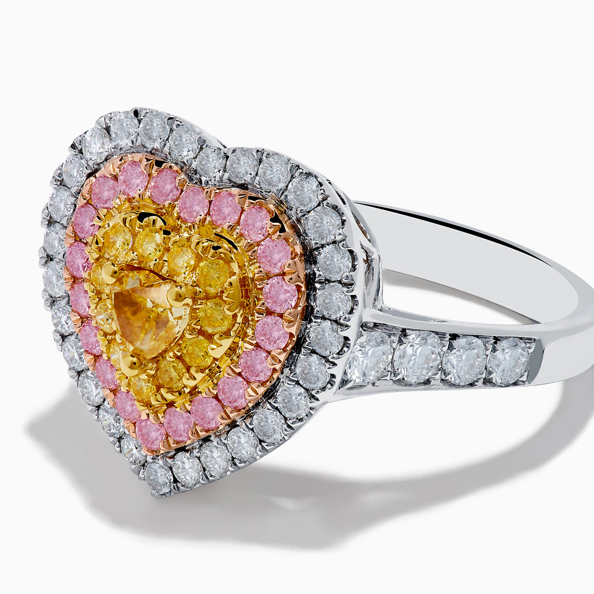 The Trio 18K Tri Color Gold White, Pink, and Yellow Diamond Heart Ring features a yellow diamond center, surrounded by pink and white diamonds on an 18K gold band for a luxurious finish.