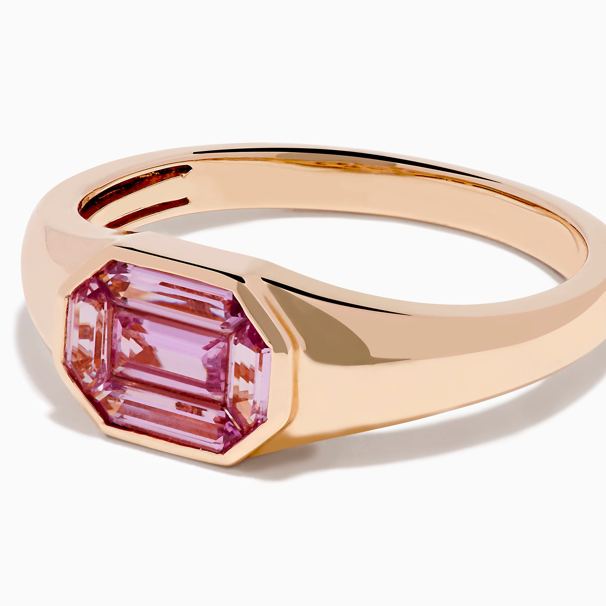 The 14K Rose Gold Bezel Set Pink Sapphire Ring showcases an emerald-cut pink sapphire in a bezel setting, presented on a white background.
