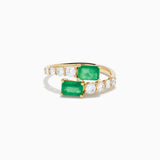 The 14K Yellow Gold Diamond and Emerald Bypass Ring features two rectangular green emeralds and rows of sparkling round white diamonds on each side in an open band design, set against a white background.