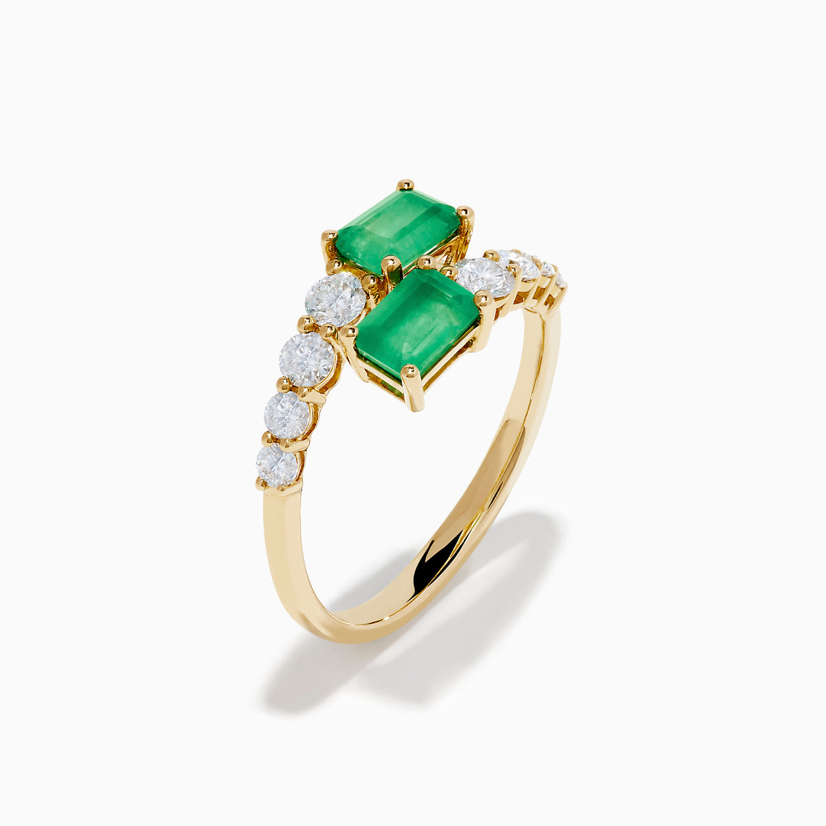 The 14K Yellow Gold Diamond and Emerald Bypass Ring features two rectangular green emeralds and rows of sparkling round white diamonds on each side in an open band design, set against a white background.