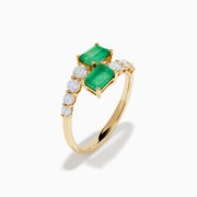 The 14K Yellow Gold Diamond and Emerald Bypass Ring features two rectangular green emeralds and rows of sparkling round white diamonds on each side in an open band design, set against a white background.
