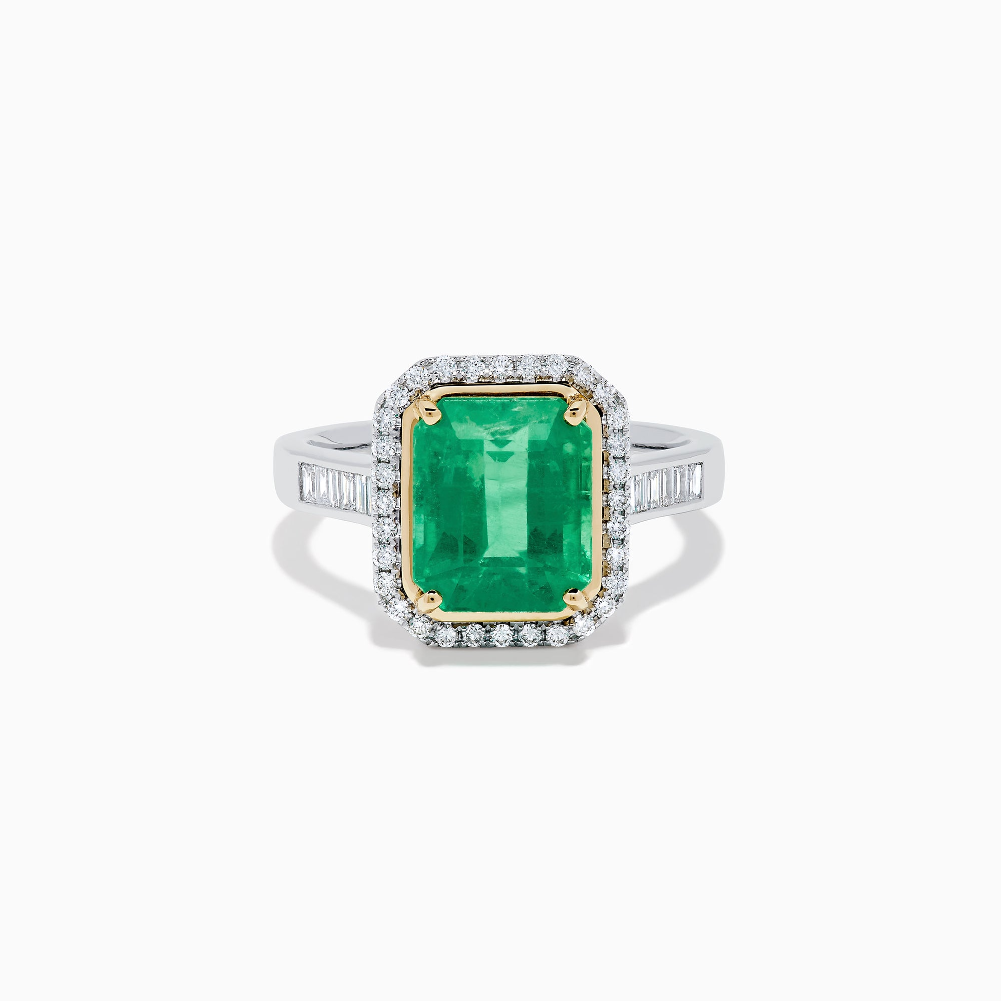 The Brasilica 14K Two Tone Gold Emerald and Diamond Ring showcases a large rectangular green emerald in a gold prong setting, accented by a halo of clear diamonds and baguette-cut diamonds along the band.