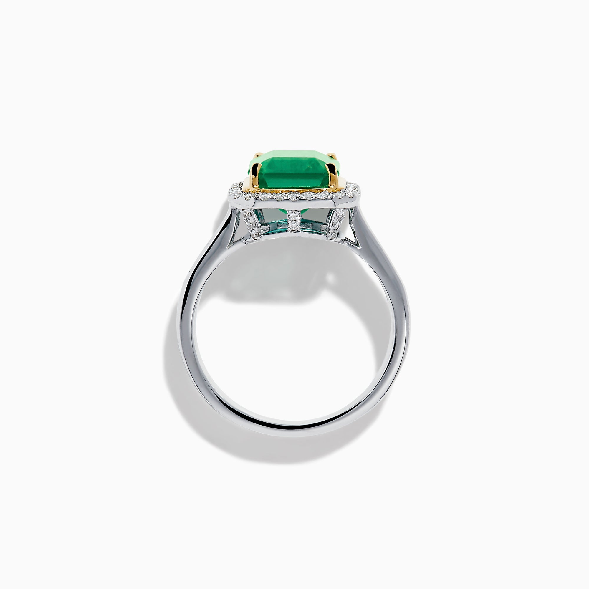 The Brasilica 14K Two Tone Gold Emerald and Diamond Ring showcases a large rectangular green emerald in a gold prong setting, accented by a halo of clear diamonds and baguette-cut diamonds along the band.
