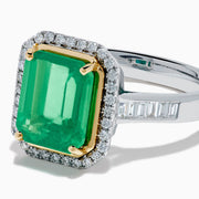 The Brasilica 14K Two Tone Gold Emerald and Diamond Ring showcases a large rectangular green emerald in a gold prong setting, accented by a halo of clear diamonds and baguette-cut diamonds along the band.