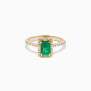 The 14K Yellow Gold Emerald and Diamond Ring showcases a rectangular emerald center stone, accented by white diamonds around the gemstone and along the band.