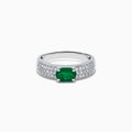 The Brasilica 14K White Gold Emerald and Diamond Ring showcases a central oval green emerald with three rows of round diamonds on each side, set in white gold and shown against a white background.