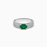 The Brasilica 14K White Gold Emerald and Diamond Ring showcases a central oval green emerald with three rows of round diamonds on each side, set in white gold and shown against a white background.