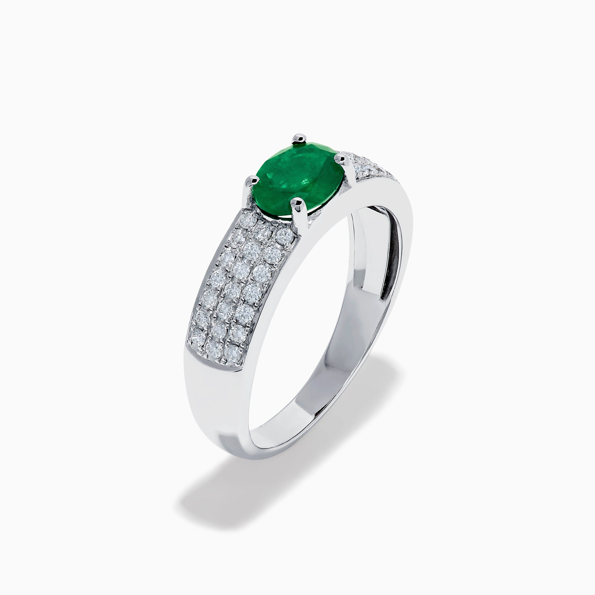 The Brasilica 14K White Gold Emerald and Diamond Ring showcases a central oval green emerald with three rows of round diamonds on each side, set in white gold and shown against a white background.