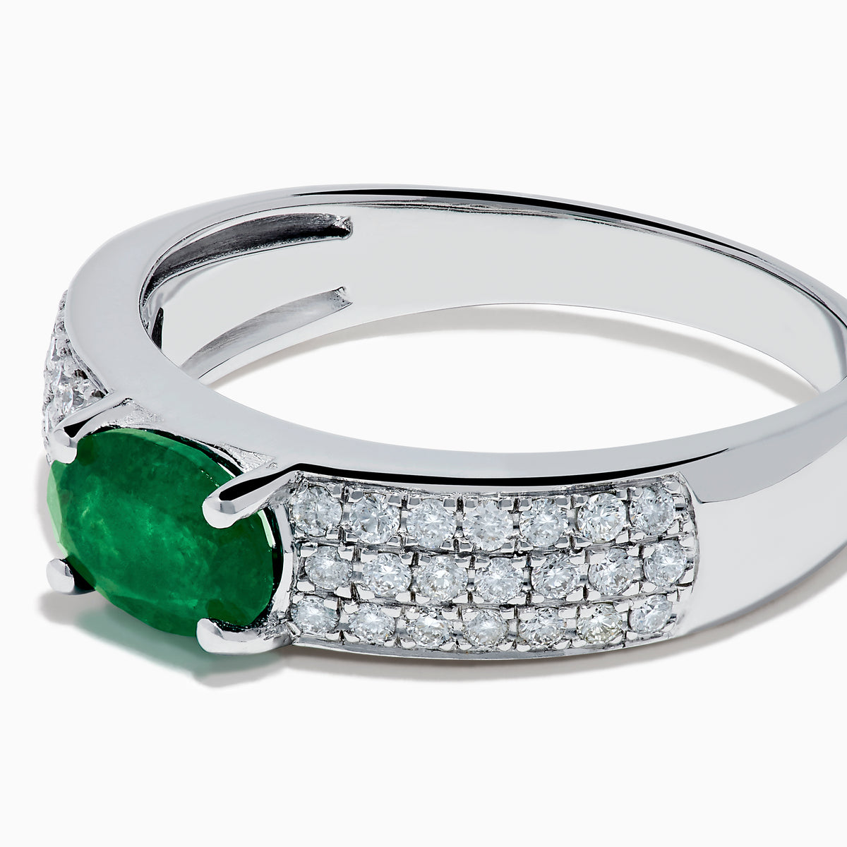 The Brasilica 14K White Gold Emerald and Diamond Ring showcases a central oval green emerald with three rows of round diamonds on each side, set in white gold and shown against a white background.