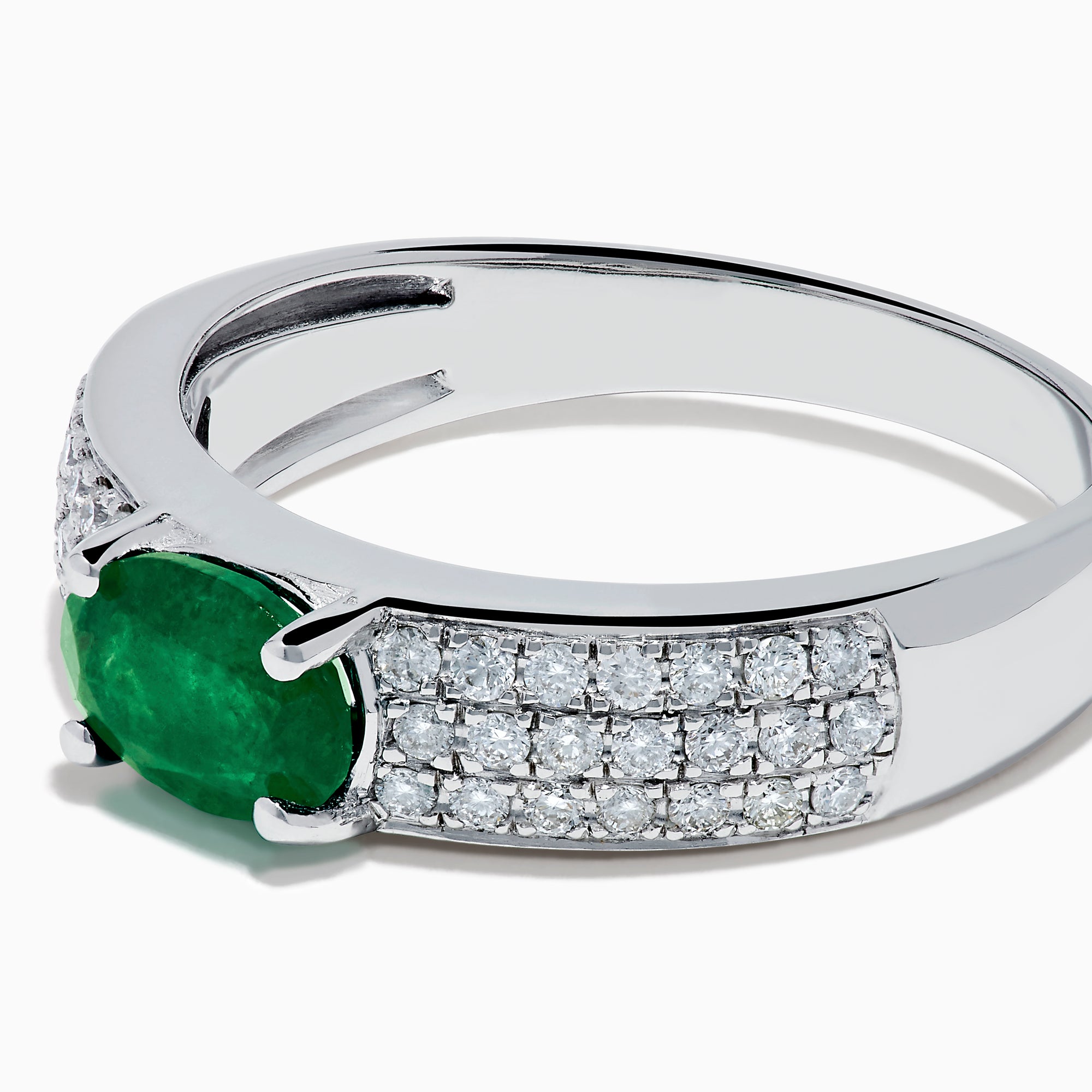 The Brasilica 14K White Gold Emerald and Diamond Ring showcases a central oval green emerald with three rows of round diamonds on each side, set in white gold and shown against a white background.