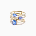 The 14K Yellow Gold Tanzanite and Diamond Multi-Row Statement Ring features three stacked bands set with white diamonds and pear, oval, and cushion-cut blue tanzanite gemstones.