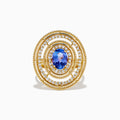 The 14K Yellow Gold Tanzanite and Diamond Concentric Halo Ring showcases concentric circular diamond bands with a central oval tanzanite gemstone, elegantly presented on a white background.