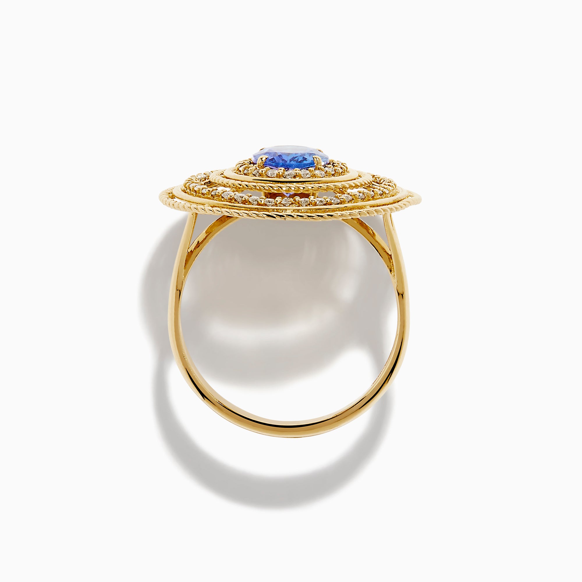 The 14K Yellow Gold Tanzanite and Diamond Concentric Halo Ring showcases concentric circular diamond bands with a central oval tanzanite gemstone, elegantly presented on a white background.