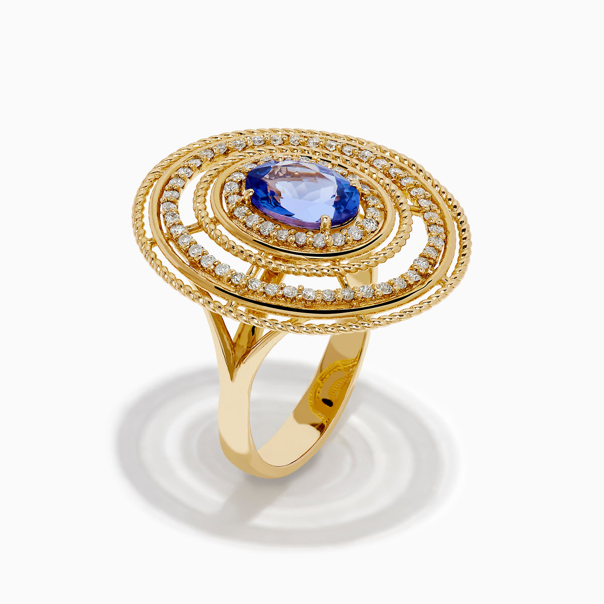The 14K Yellow Gold Tanzanite and Diamond Concentric Halo Ring showcases concentric circular diamond bands with a central oval tanzanite gemstone, elegantly presented on a white background.