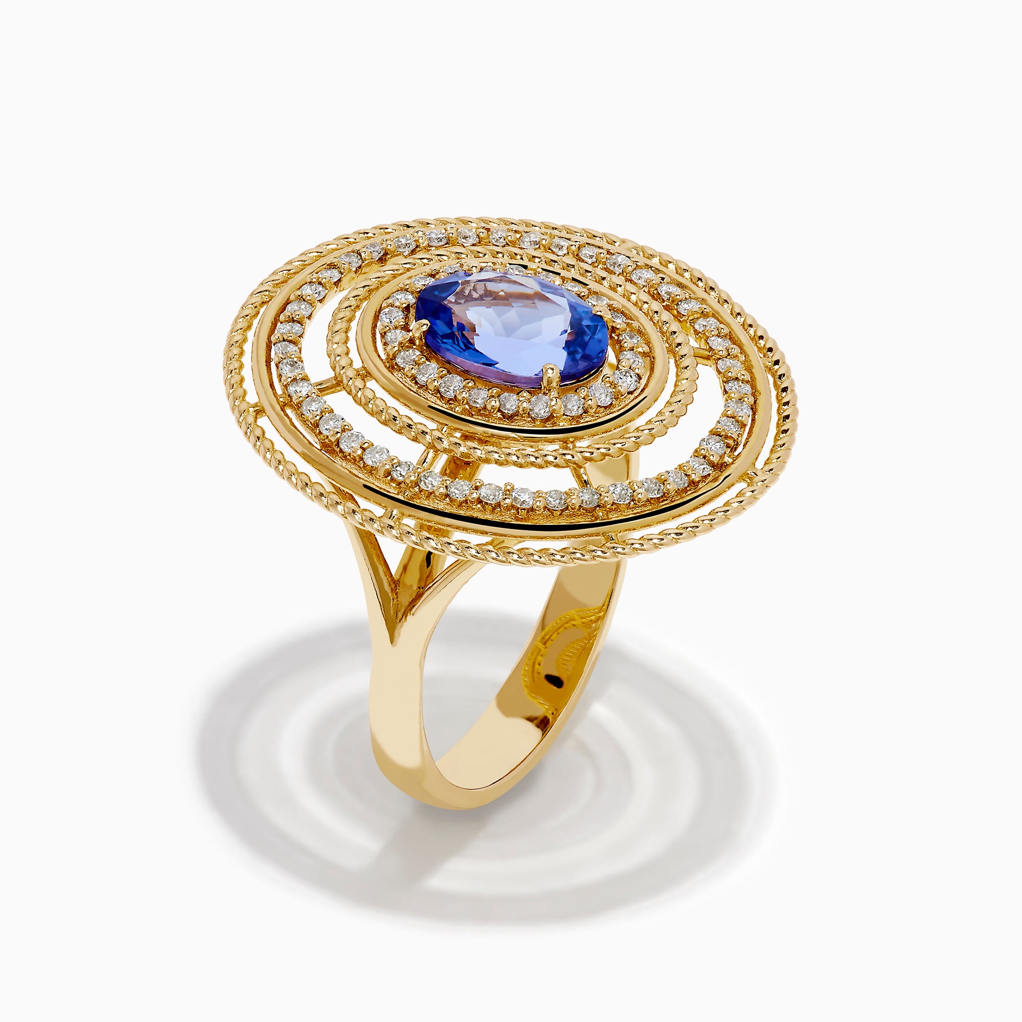 The 14K Yellow Gold Tanzanite and Diamond Concentric Halo Ring showcases concentric circular diamond bands with a central oval tanzanite gemstone, elegantly presented on a white background.