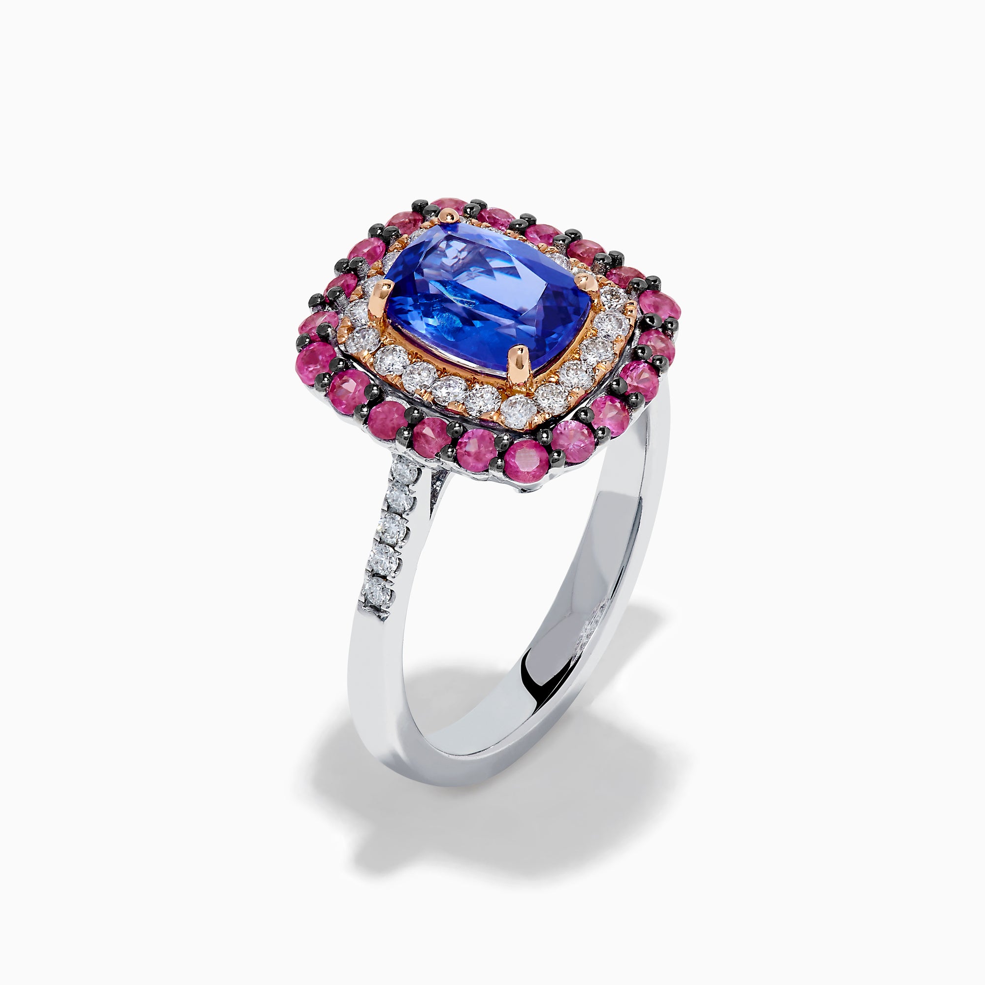 The 14K Two Tone Gold Tanzanite, Diamond, and Pink Sapphire Cushion Halo Ring features a striking tanzanite center, framed by sparkling diamonds and a halo of vivid pink sapphires on a sleek white background.