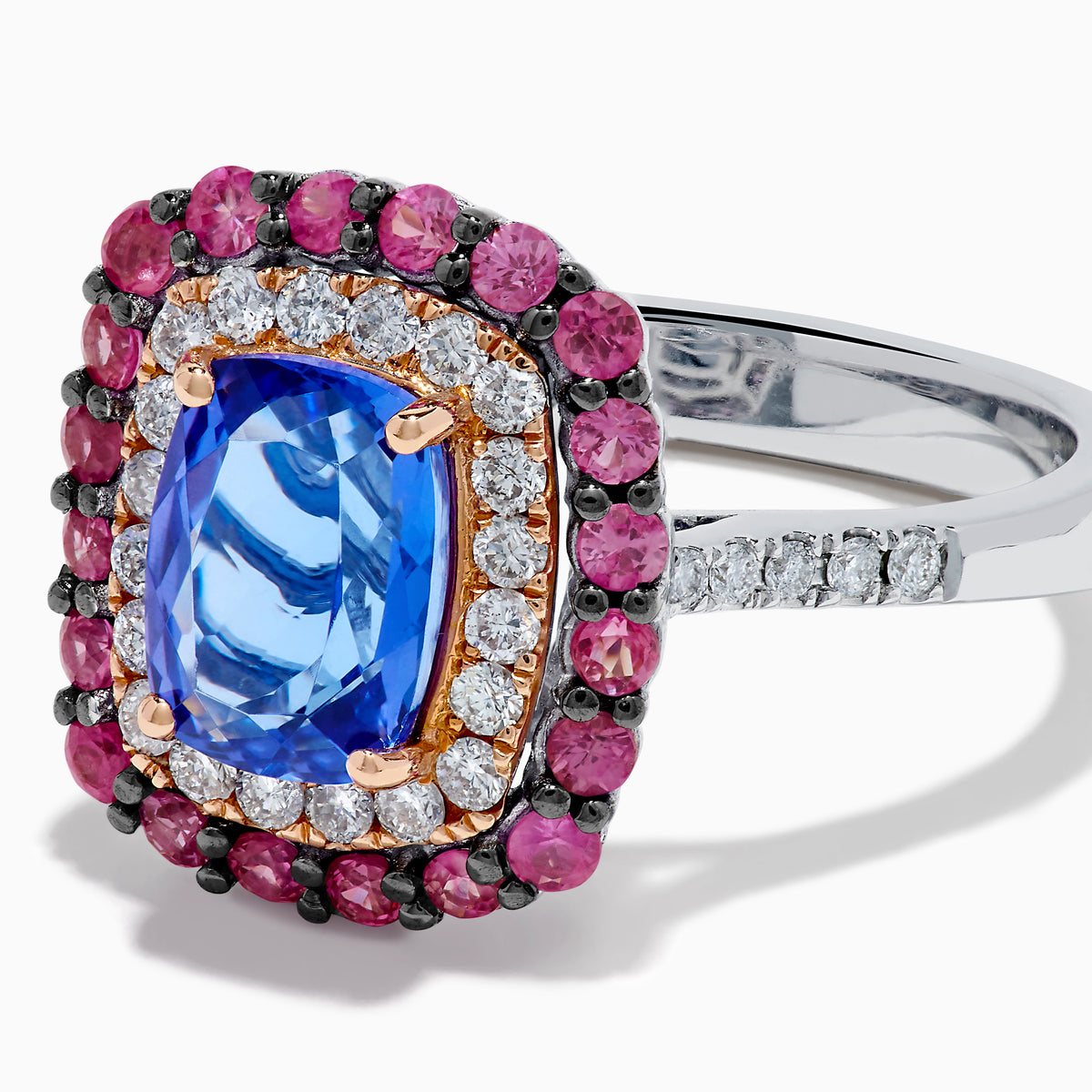 The 14K Two Tone Gold Tanzanite, Diamond, and Pink Sapphire Cushion Halo Ring features a striking tanzanite center, framed by sparkling diamonds and a halo of vivid pink sapphires on a sleek white background.