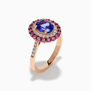 The 14K Rose Gold Tanzanite, Diamond, and Pink Sapphire Oval Halo Ring features a large oval blue tanzanite center, double halos of white diamonds and pink sapphires, plus diamond accents on the band.