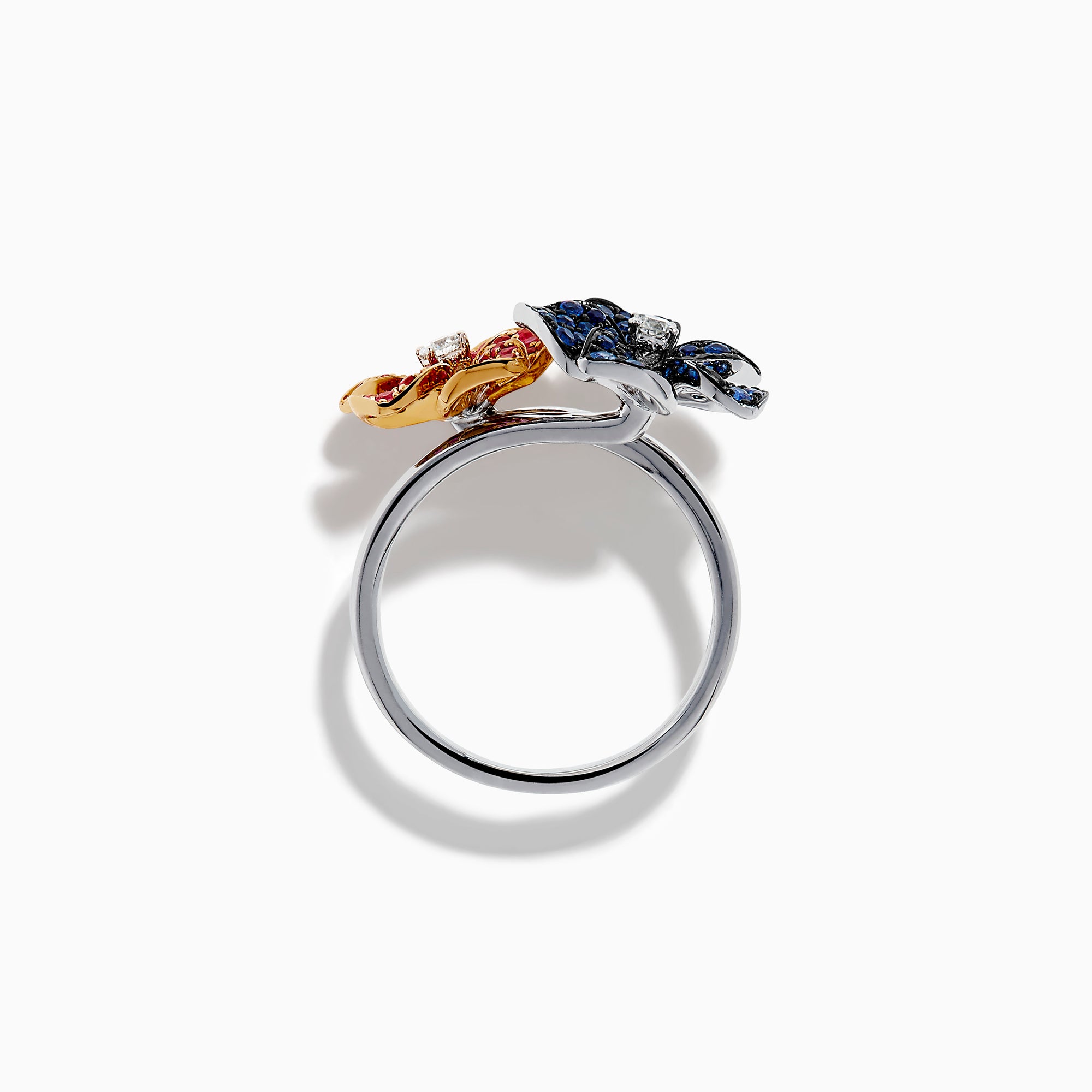 The 14K Two Tone Ruby, Sapphire, and Diamond Floral Bypass Ring features jeweled floral designs with ruby, sapphire, and diamond accents, displayed elegantly on a white background.