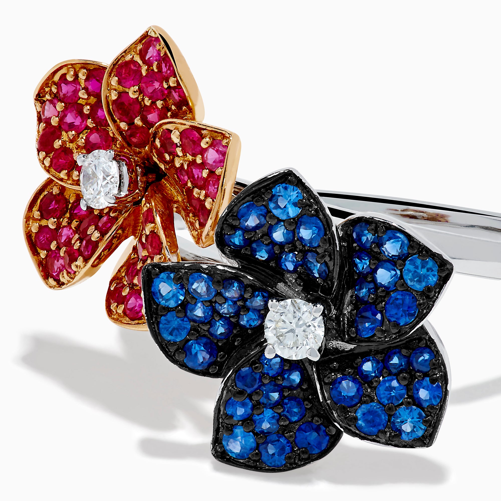 The 14K Two Tone Ruby, Sapphire, and Diamond Floral Bypass Ring features jeweled floral designs with ruby, sapphire, and diamond accents, displayed elegantly on a white background.