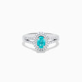 The 18K White Gold Paraiba and Diamond Ring showcases an oval Paraiba gemstone at the center, encircled by a halo of sparkling diamonds and accented with additional diamonds along its elegant split shank band.