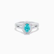 The 18K White Gold Paraiba and Diamond Ring showcases an oval Paraiba gemstone at the center, encircled by a halo of sparkling diamonds and accented with additional diamonds along its elegant split shank band.