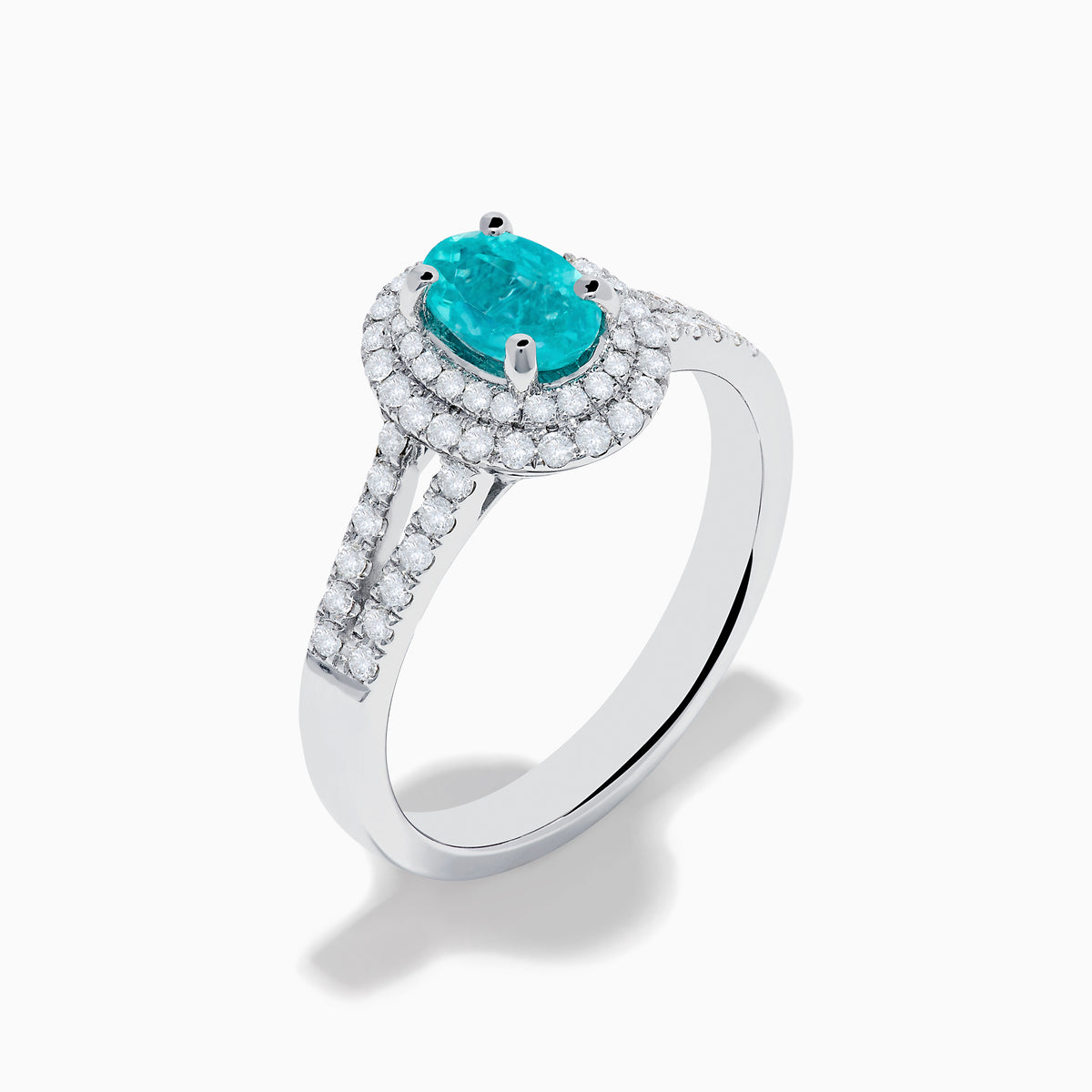 The 18K White Gold Paraiba and Diamond Ring showcases an oval Paraiba gemstone at the center, encircled by a halo of sparkling diamonds and accented with additional diamonds along its elegant split shank band.