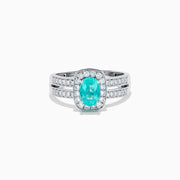 The 18K White Gold Paraiba and Diamond Halo Ring features an oval Paraiba center gemstone, encircled by sparkling diamonds and set on an elegant split shank band adorned with additional diamonds.