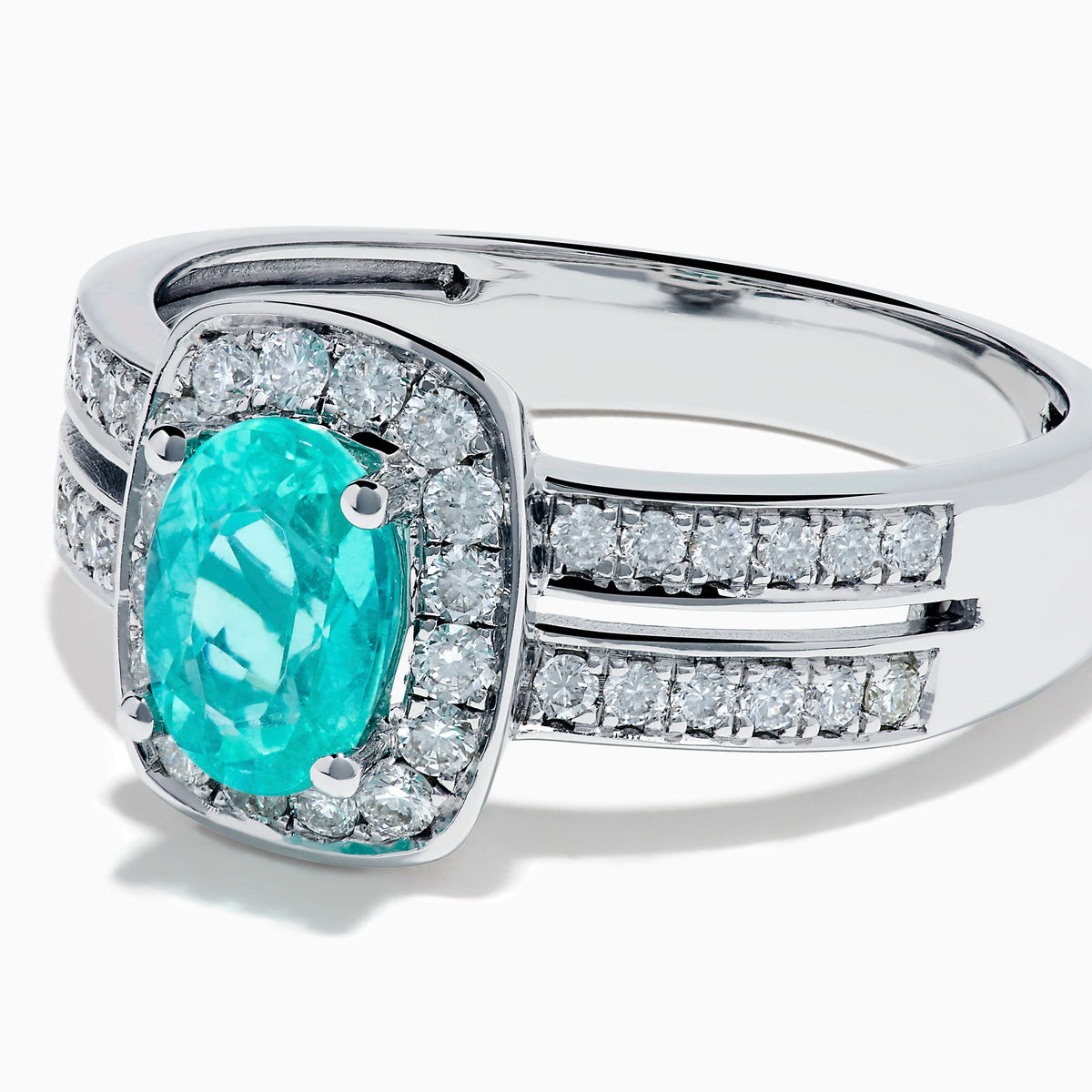 The 18K White Gold Paraiba and Diamond Halo Ring features an oval Paraiba center gemstone, encircled by sparkling diamonds and set on an elegant split shank band adorned with additional diamonds.