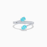 The 18K White Gold Paraiba and Diamond Bypass Ring features two oval Paraiba gemstones at each end of an open band, accented with small sparkling diamonds along the upper surface.