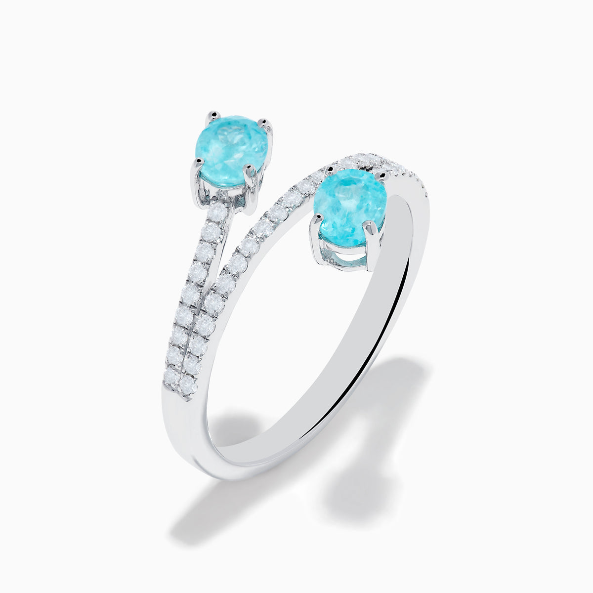 The 18K White Gold Paraiba and Diamond Bypass Ring features two oval Paraiba gemstones at each end of an open band, accented with small sparkling diamonds along the upper surface.